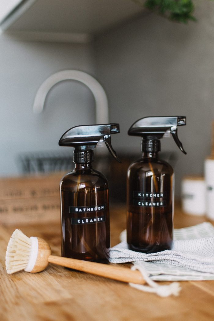 two spray bottles with bathroom cleaner and kitchen cleaner with a scrub brush