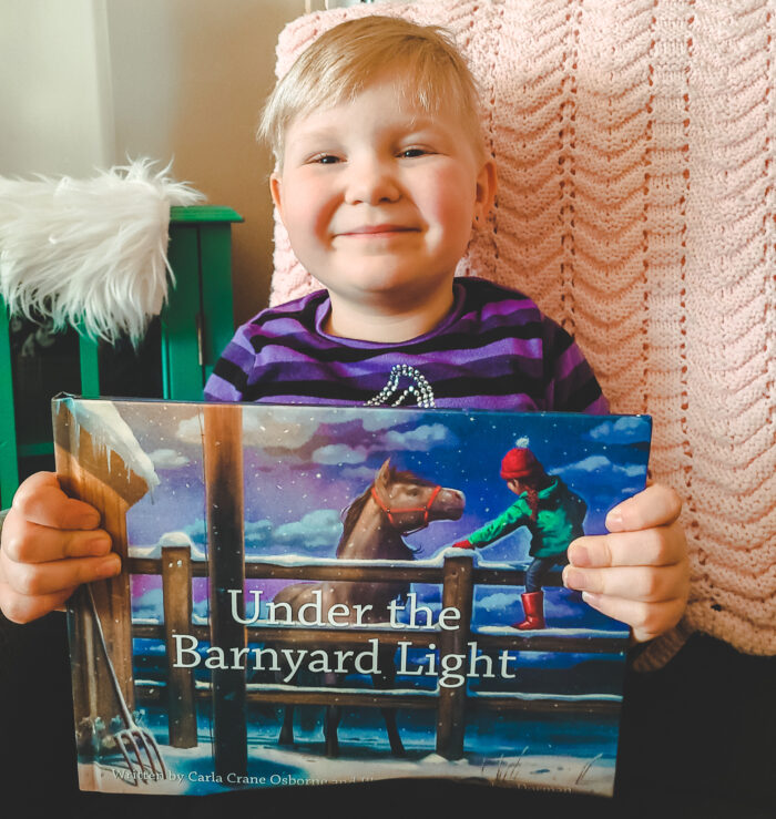 child holding up Under the Barnyard Light by Carla Crane Osborne
