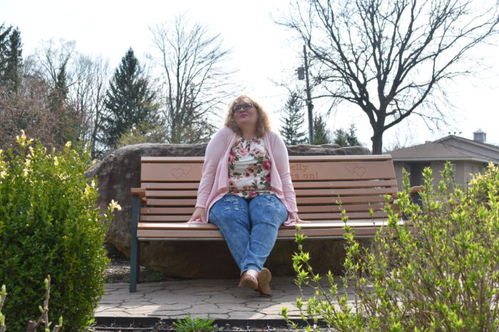 person in pink cardigan, jeans, and floral shirt looking in deep thought