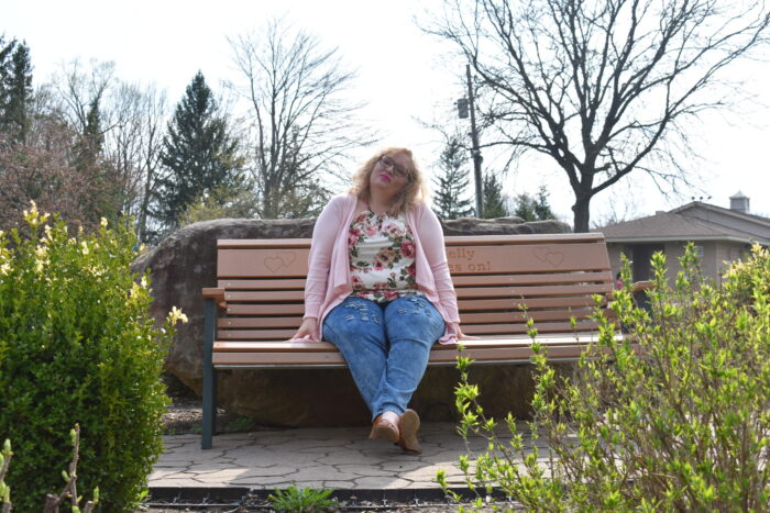 person in pink cardigan, jeans, and floral shirt looking in deep thought