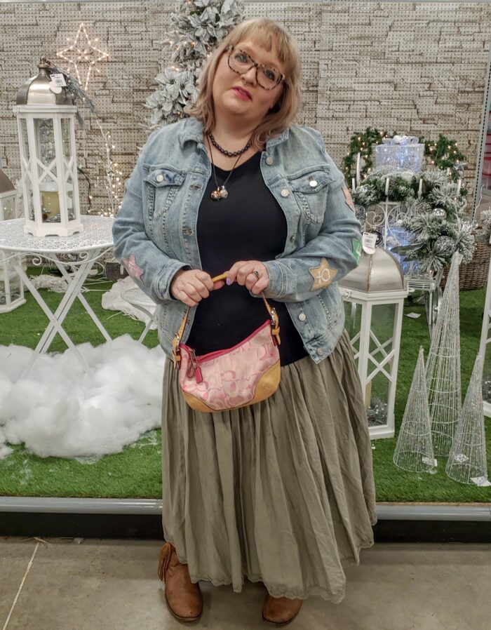 person wearing denim jacket, black tee, skirt, and carrying a designer purse