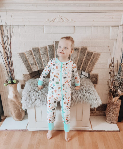 toddler wearing romper from Three Coastal Babies standing in front of fire place