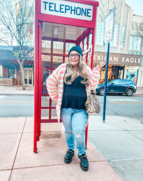 person standing in front of telephone booth wearing thrifted clothing