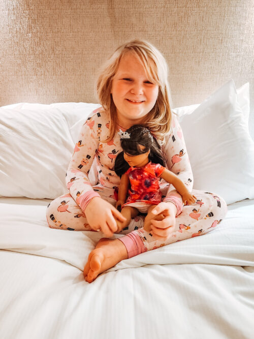 child wearing Three coastal Babies pajamas and holding an american girl doll