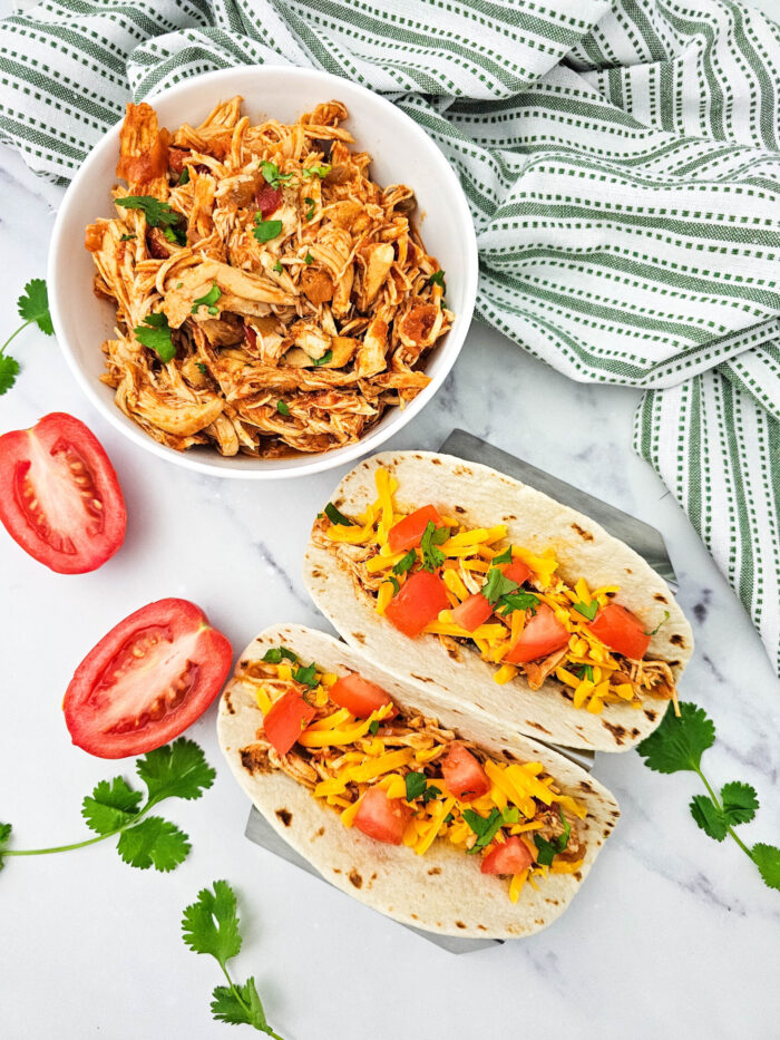 crockpot salsa chicken tacos with tomatoes and garnish near a green and white cloth