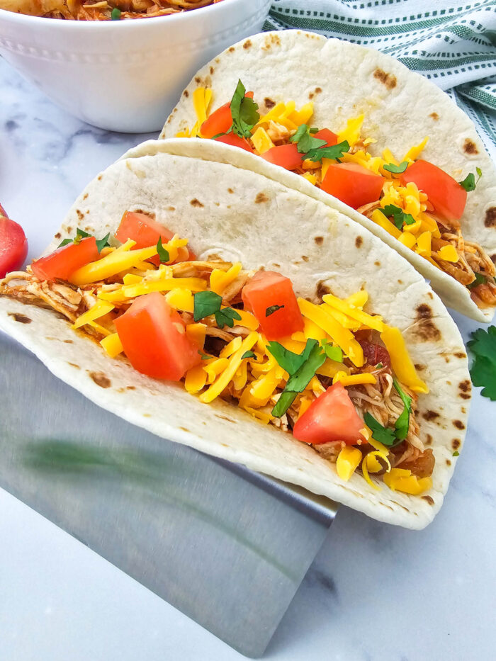 crockpot salsa chicken tacos with tomatoes and garnish near a green and white cloth